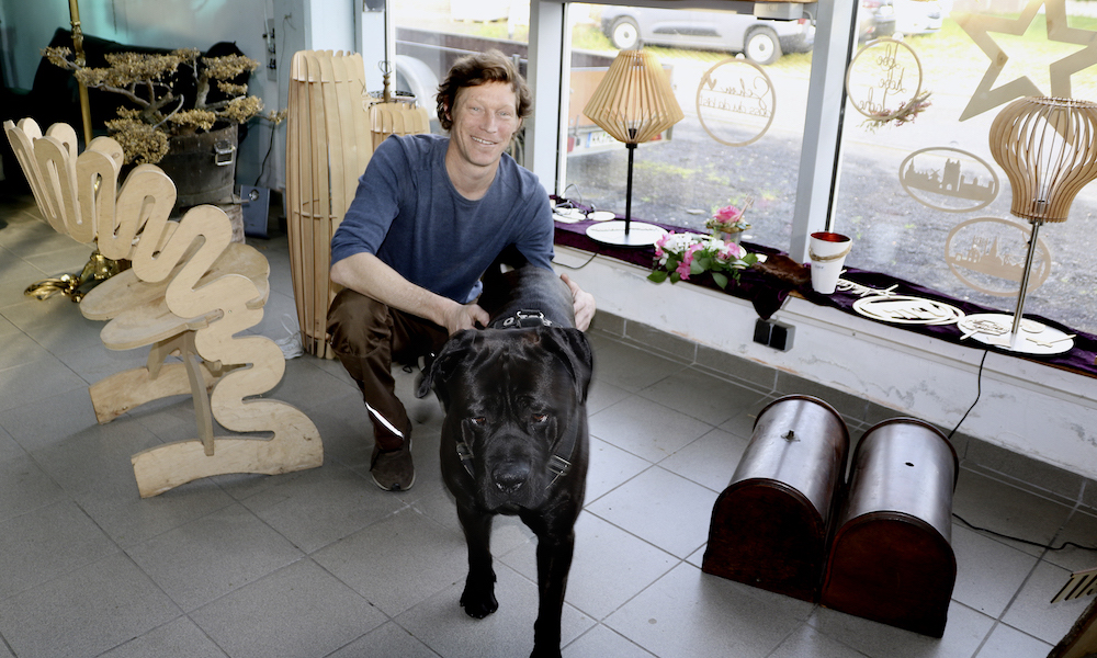 Inhaber Oliver Pollan mit Hund Polo in seinem Geschäft Holzikat.
