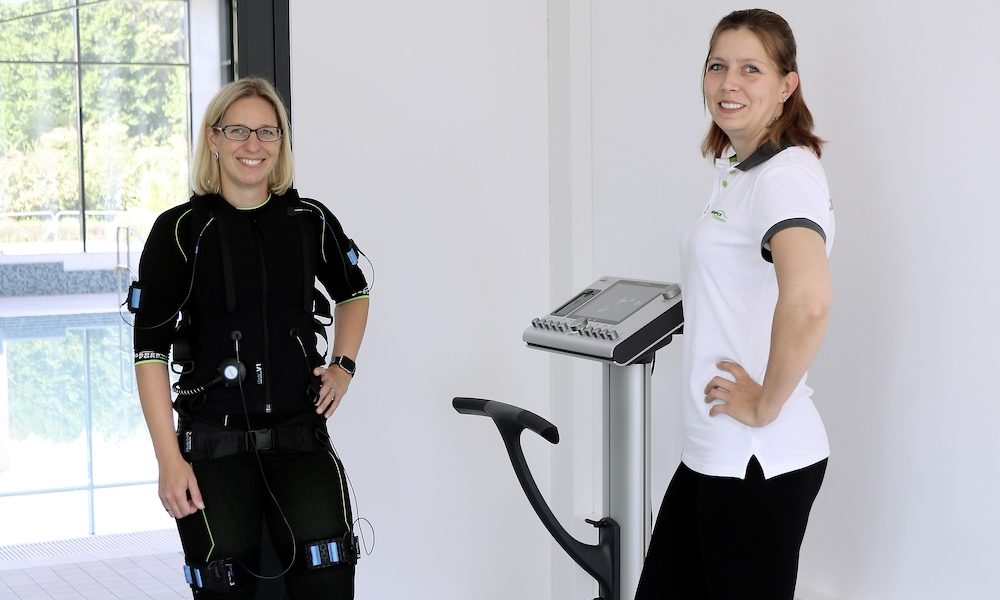 Zwei Frauen stehen nebeneinander, eine in einem speziellen Anzug für ein EMS-Training.