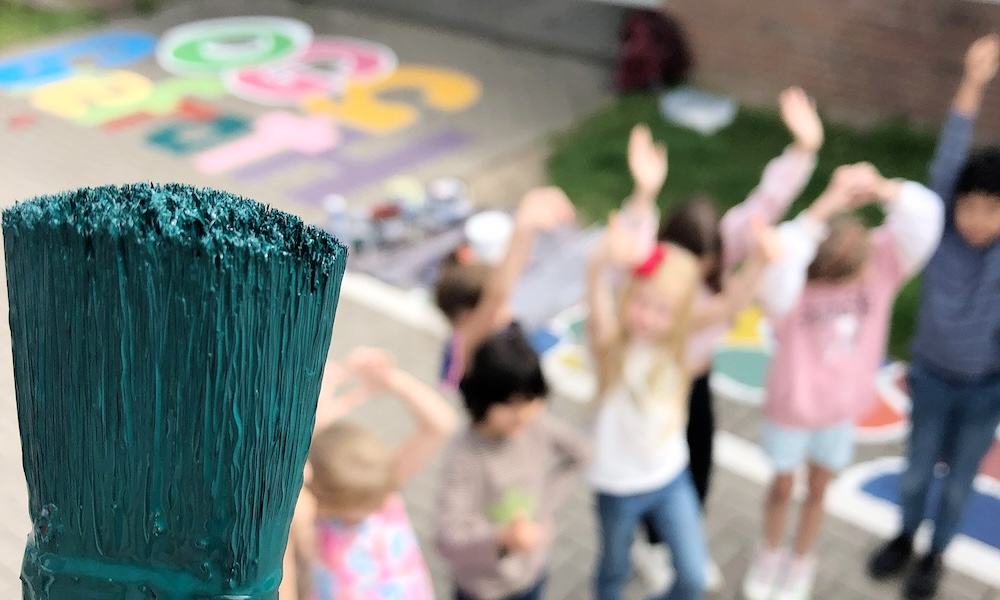 Farbiger Pinsel im Vordergrund und unscharf im Hintergrund ein paar Grundschulkinder